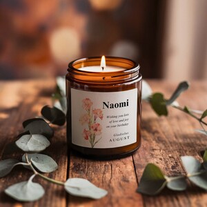 May include: A brown glass candle with a white label that says "Naomi" and "Wishing you lots of love and joy on your birthday". The label also includes a floral illustration and the text "Gladiolus AUGUST".