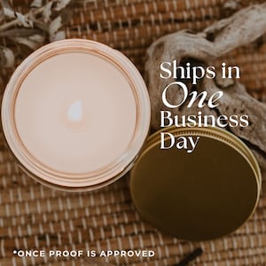 May include: A close-up of a lit candle in a glass jar with a gold lid. The candle is surrounded by a woven mat. The text "Ships in One Business Day" is written in white on a brown background.