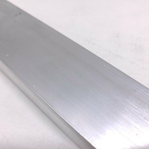 Puede incluir: Primer plano de una barra de metal plateado cepillado. La barra tiene un acabado liso y pulido y es de forma rectangular.