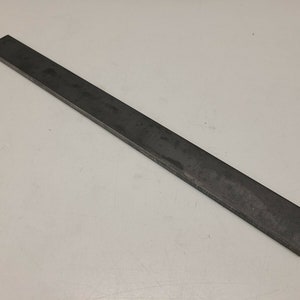 May include: A long, rectangular, dark gray metal bar. The bar is straight with a flat surface and appears to be made of steel. The item is likely a component for construction or repair.
