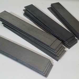 May include: Four stacks of flat metal bars, each stack is a different height. The bars are a dark gray color.
