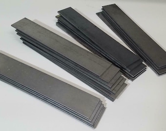May include: Four stacks of flat metal bars, each stack is a different height. The bars are a dark gray color.