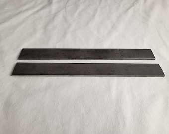 May include: Two rectangular, dark gray metal plates with beveled edges are displayed against a white background. The plates are parallel to each other, suggesting they are components of a larger item or project.