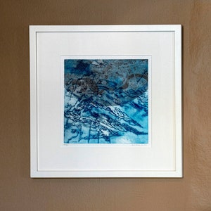 May include: A framed abstract print with blue and gray tones. The print features a swirling, organic pattern reminiscent of water or clouds.