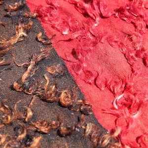 Puede incluir: Primer plano de una tela con dos texturas diferentes. Un lado es de color marrón oscuro con una textura peluda, y el otro lado es de color rojo brillante con una textura peluda similar.