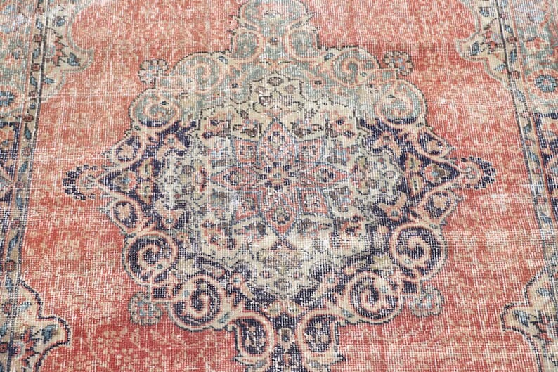 Pode incluir: Um tapete retangular com um fundo laranja terracota desbotado e um grande medalh&atilde;o central em azul-marinho, creme e verde-s&aacute;lvia. O padr&atilde;o intrincado inclui motivos florais sim&eacute;tricos e detalhes de vinhas entrela&ccedil;adas.