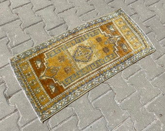 Puede incluir: Una alfombra turca vintage con un patrón geométrico amarillo y marrón. La alfombra tiene un aspecto descolorido y desgastado, perfecto para añadir un toque de estilo bohemio a tu hogar.