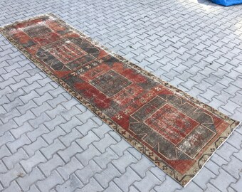 May include: A vintage runner rug with a faded red, brown, and cream color scheme. The rug has a geometric pattern with a central medallion.