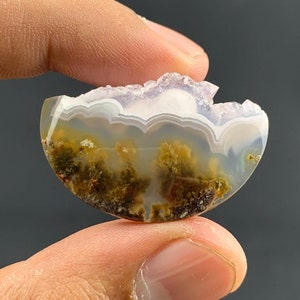 May include: A half-round agate cabochon with a white and light purple banded top and a green and brown dendritic pattern on the bottom.
