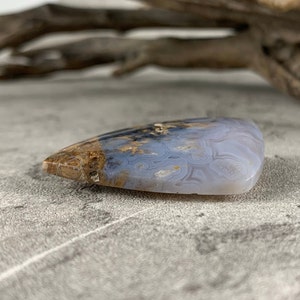 May include: A light blue and brown agate cabochon with a swirling pattern. The cabochon is shaped like a teardrop and has a smooth, polished surface.