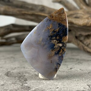 May include: A light blue agate cabochon with brown and black dendritic patterns. The cabochon is cut in a teardrop shape and is approximately 2 inches long.