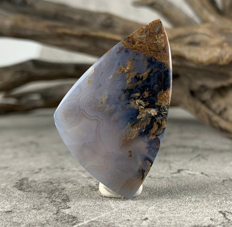 May include: A light blue agate cabochon with brown and black dendritic patterns. The cabochon is cut in a teardrop shape and is approximately 2 inches long.
