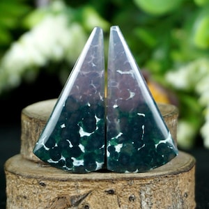 May include: Two triangular polished gemstones featuring a deep forest green base colour with dark circular inclusions and white vein-like patterns throughout the surface. The stones have a smooth, reflective finish and are shaped into matching wedges.