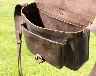 Op de afbeelding: Bruine leren messenger bag met een klepsluiting en verstelbare schouderriem. De tas heeft meerdere vakken, een messing gesp en zichtbare stikseldetails. De tas is open en onthult de binnenkant en extra vakken.