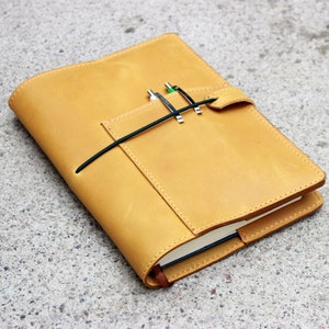 May include: A tan leather notebook cover with a pen holder and a flap closure.