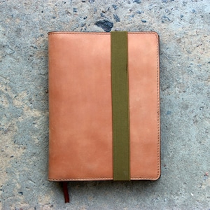May include: A tan leather notebook with a green elastic band closure.