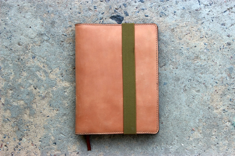 May include: A tan leather notebook with a green elastic band closure.