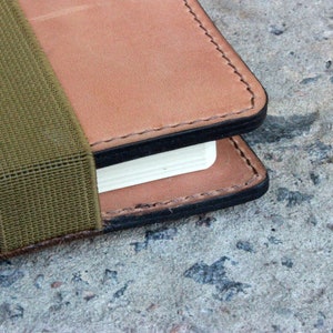 May include: A brown leather notebook with a green elastic band closure. The notebook has a black stitched edge and a white page showing.