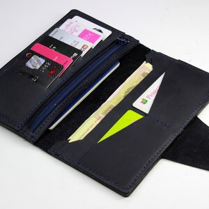 Peut inclure: Un portefeuille en cuir bleu foncé avec un compartiment zippé, plusieurs emplacements pour cartes et un rabat avec une fermeture à pression. Le portefeuille est ouvert et contient plusieurs cartes de crédit, de l'argent liquide et une carte verte avec le mot "Россия" imprimé dessus.