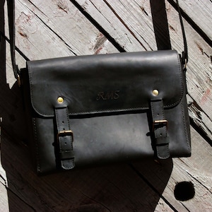 May include: A black leather messenger bag with gold buckles and a personalized inscription that reads "RMS".