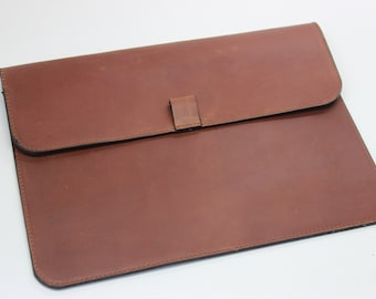 May include: A brown leather laptop sleeve with a flap closure and a small strap.
