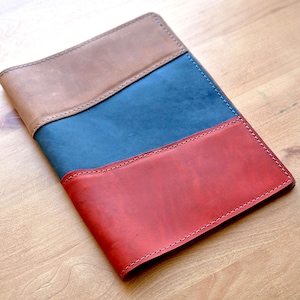 May include: A leather notebook cover with three sections of different colors: brown, blue, and red. The cover is stitched together with a decorative stitch.