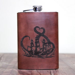 May include: A brown leather flask with a silver top and a black engraved design of an octopus attacking a ship.
