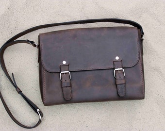 May include: A brown leather messenger bag with two silver buckles and a long adjustable strap.