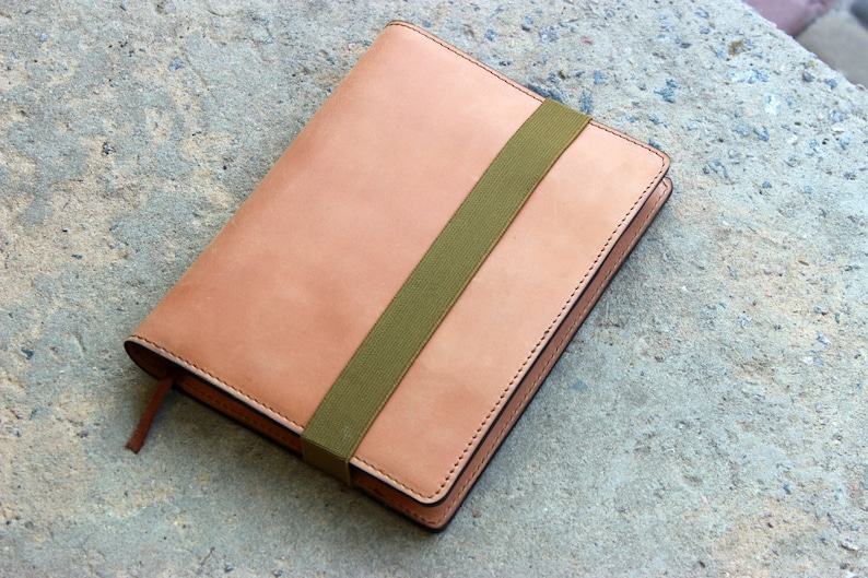 May include: A tan leather notebook with a green elastic band closure.