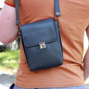 May include: A person wearing a brown t-shirt with a blue leather crossbody bag. The bag has a silver clasp and a brown strap.