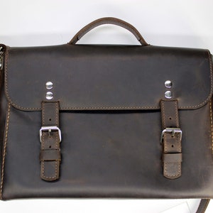 May include: A brown leather briefcase with two buckles and a shoulder strap. The briefcase has a top handle and is made of a distressed leather.