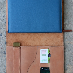 May include: A brown leather notebook cover with a blue insert and a credit card and a small green card tucked into the pockets. The credit card has the text "Sberbank" and the number "4149 457..." printed on it.
