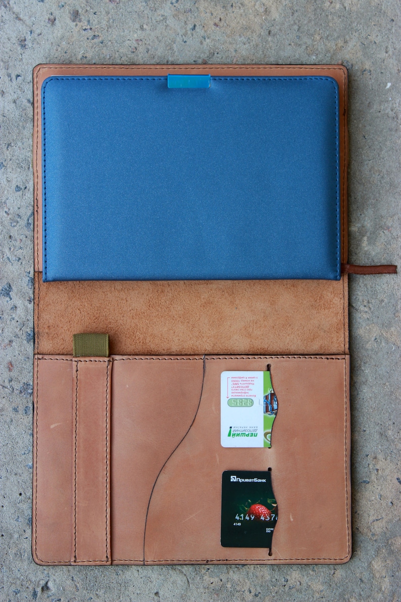 May include: A brown leather notebook cover with a blue insert and a credit card and a small green card tucked into the pockets. The credit card has the text "Sberbank" and the number "4149 457..." printed on it.