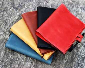 Könnte beinhalten: Ein Stapel von fünf ledergebundenen Notizbüchern in verschiedenen Farben, darunter Rot, Gelb, Blau, Braun und Schwarz. Die Notizbücher sind fächerförmig angeordnet, wobei das rote Notizbuch oben liegt. Die Notizbücher sind alle geschlossen und haben ein schlichtes, elegantes Design.
