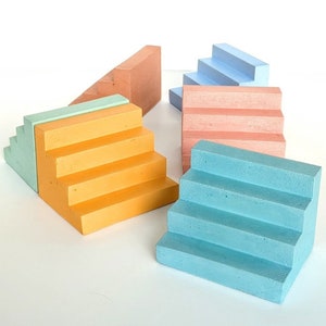 May include: Five miniature concrete steps in different colours. The steps are in shades of blue, pink, yellow, and green. The steps are arranged in a staggered pattern.