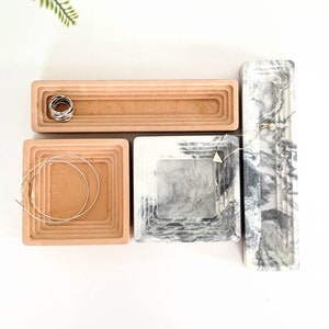 May include: Four decorative trays, two in a light brown colour and two in a grey and white marble pattern. The trays are stacked in a concentric circle design. The trays are perfect for organising jewellery or other small items.