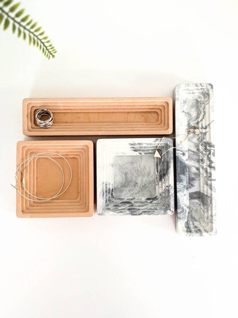 May include: Four decorative trays, two in a light brown colour and two in a grey and white marble pattern. The trays are stacked in a concentric circle design. The trays are perfect for organising jewellery or other small items.