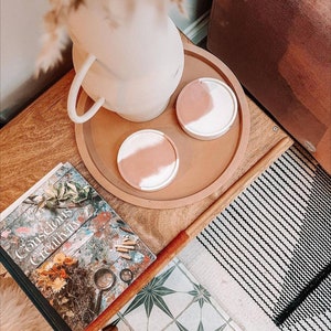 Könnte beinhalten: Ein Holztisch mit einem Buch mit dem Titel "Conscious Creativity" und zwei rosa und weißen Betonuntersetzern auf einem braunen Tablett.