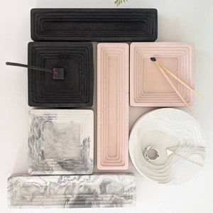 May include: Set of six concrete trays in various shapes and sizes. The trays are in black, white, and pink with a marbled pattern. The trays are ideal for organising small items, such as jewellery, keys, or incense.