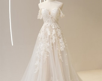 May include: A white off-the-shoulder wedding dress with a lace bodice and a tulle skirt. The dress has a flowing silhouette and delicate floral embroidery.