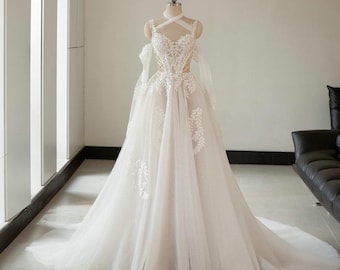May include: A white wedding dress with a flowing skirt and a long train. The bodice features intricate lace detailing and a halter neckline. The dress is displayed on a mannequin in a well-lit room.
