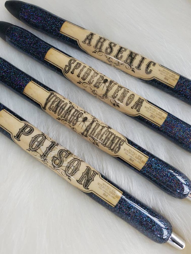 May include: Four black glitter pens with vintage-style labels that read "Arsenic", "Spider Venom", "Venomous Arachnis", and "Poison". Each label has the text "Wicked Way Witching Supplies" and the year "1814".