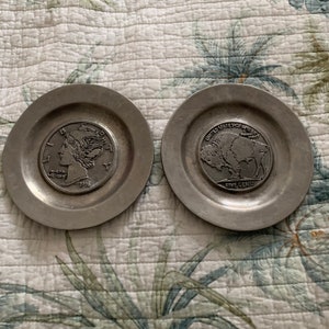 May include: Two silver-colored metal coasters with raised images of coins. The left coaster features a 1916 Mercury dime with the profile of Liberty. The right coaster features a 1938 Buffalo nickel with the profile of a buffalo.
