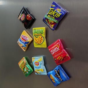Op de afbeelding: Een verzameling miniatuur snackzakmagneten, waaronder Lay's, Fritos, Funyuns, Sun Chips, Doritos en Takis. De zakken zijn in verschillende kleuren, zoals blauw, geel, rood en groen, en voorzien van merknamen en tekst.