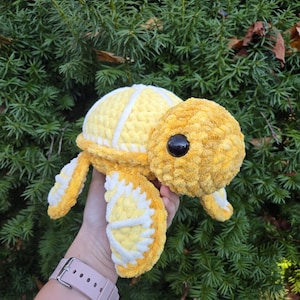 May include: A crocheted yellow and white turtle plush toy. The turtle has a textured shell and large black eyes.