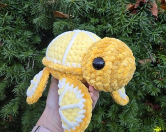 May include: A crocheted yellow and white turtle plush toy. The turtle has a textured shell and large black eyes.