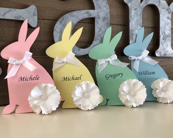 May include: Four pastel colored paper bunny rabbits with white bows and white paper flowers. The bunnies are labeled "Michele", "Michael", "Gregory", and "William".