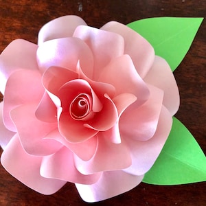 May include: A pink paper flower with a curled center and two green leaves.