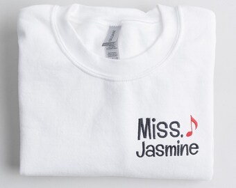 May include: White sweatshirt with the text "Miss. Jasmine" embroidered in navy blue with a red musical note.