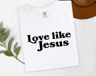 May include: White t-shirt with black text that reads "Love like Jesus" in a retro font.